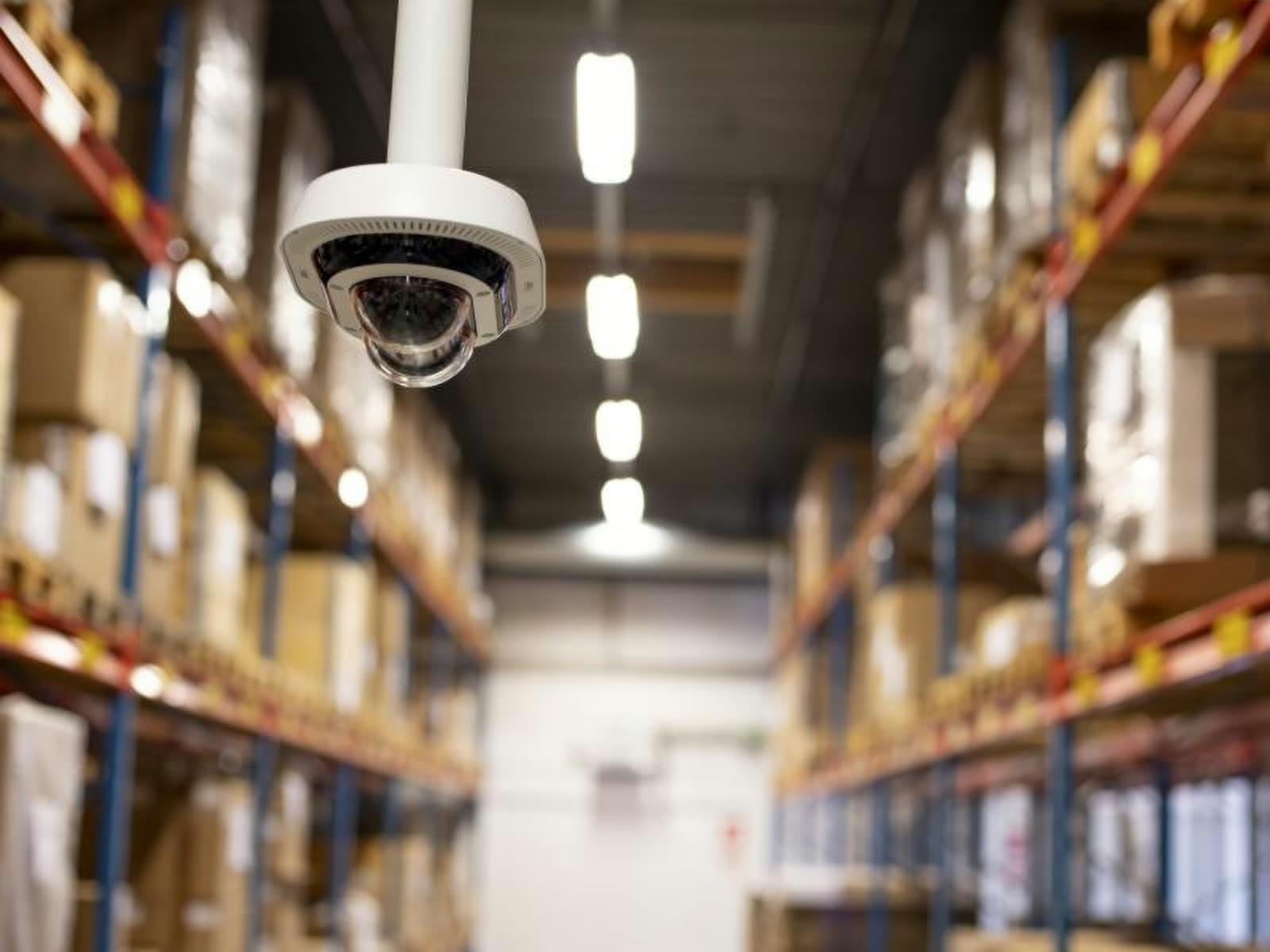 A dome camera mounted above a racking aisle inside an operating warehouse