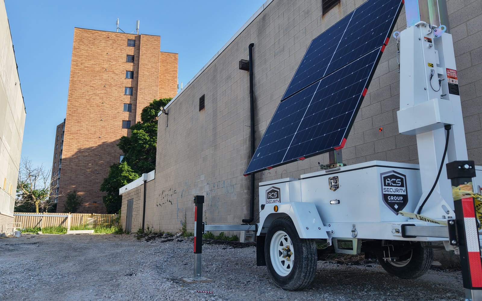 An ACS mobile tower on a gravel lot beside a commercial building, solar panel deployed