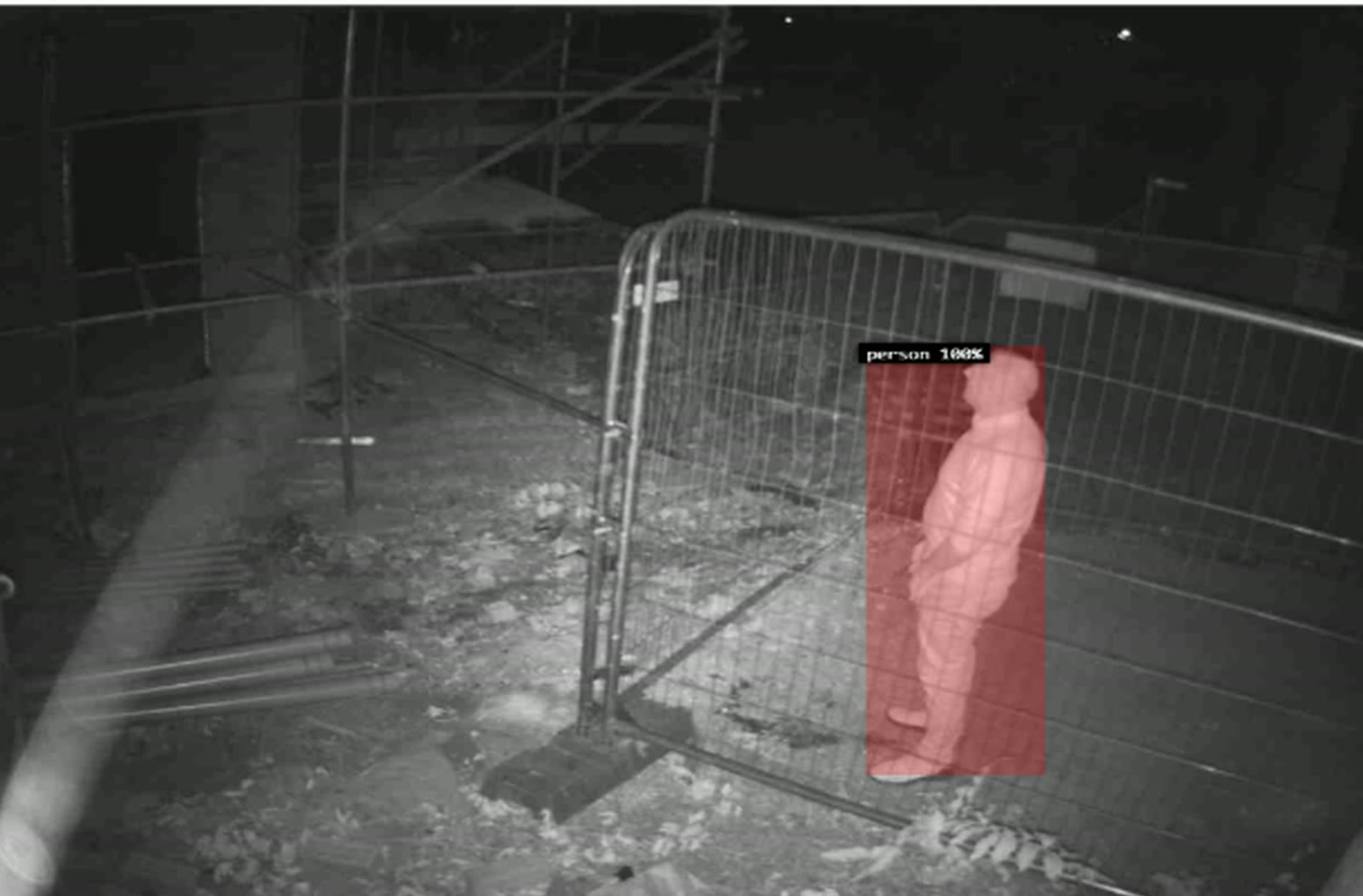 A night camera frame from an ACS site: a person at a site fence, boxed and labelled by the detection