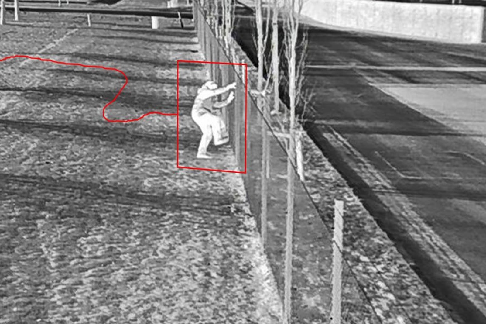 A thermal camera frame from an ACS site at night: a person climbing a fence, tracked and outlined in red