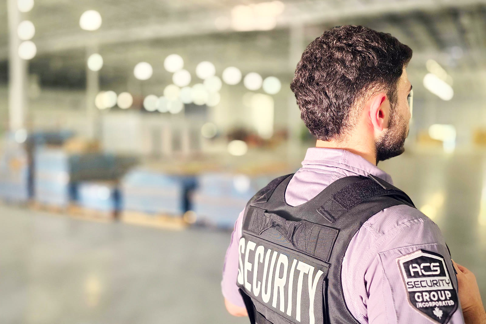 An ACS officer on the floor of an operating warehouse, racking and lit aisles behind