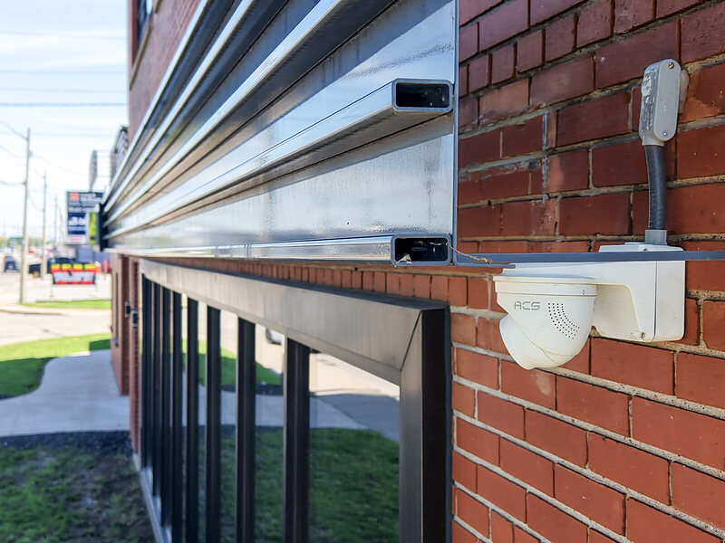ACS dome camera mounted under a metal awning on a brick commercial building beside a street