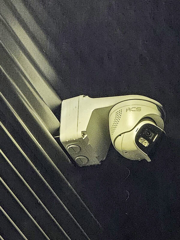 ACS turret camera on a wall bracket, lit against a dark wall at night