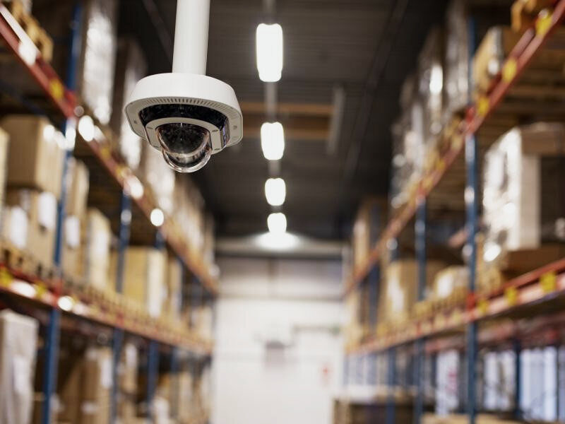 Dome camera on the ceiling of a warehouse aisle between stocked shelves