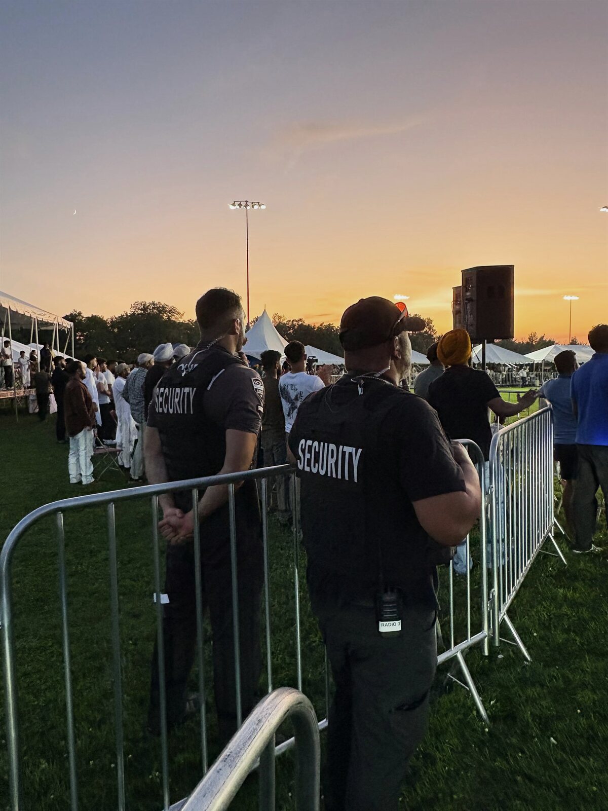 Two ACS security guards at a crowd barrier during an outdoor event at sunset