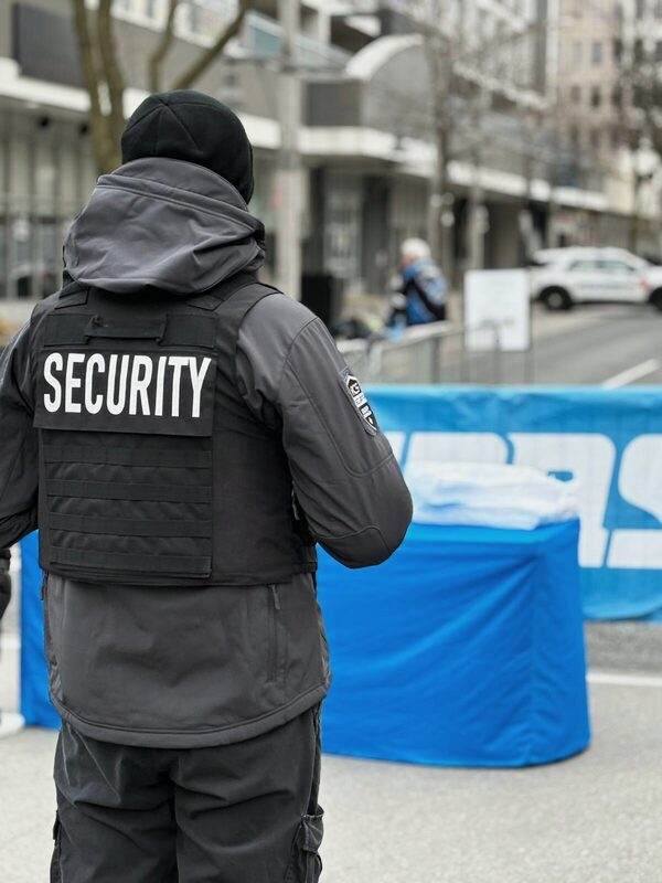 ACS security guard in a security vest on a downtown street beside a blue event tent