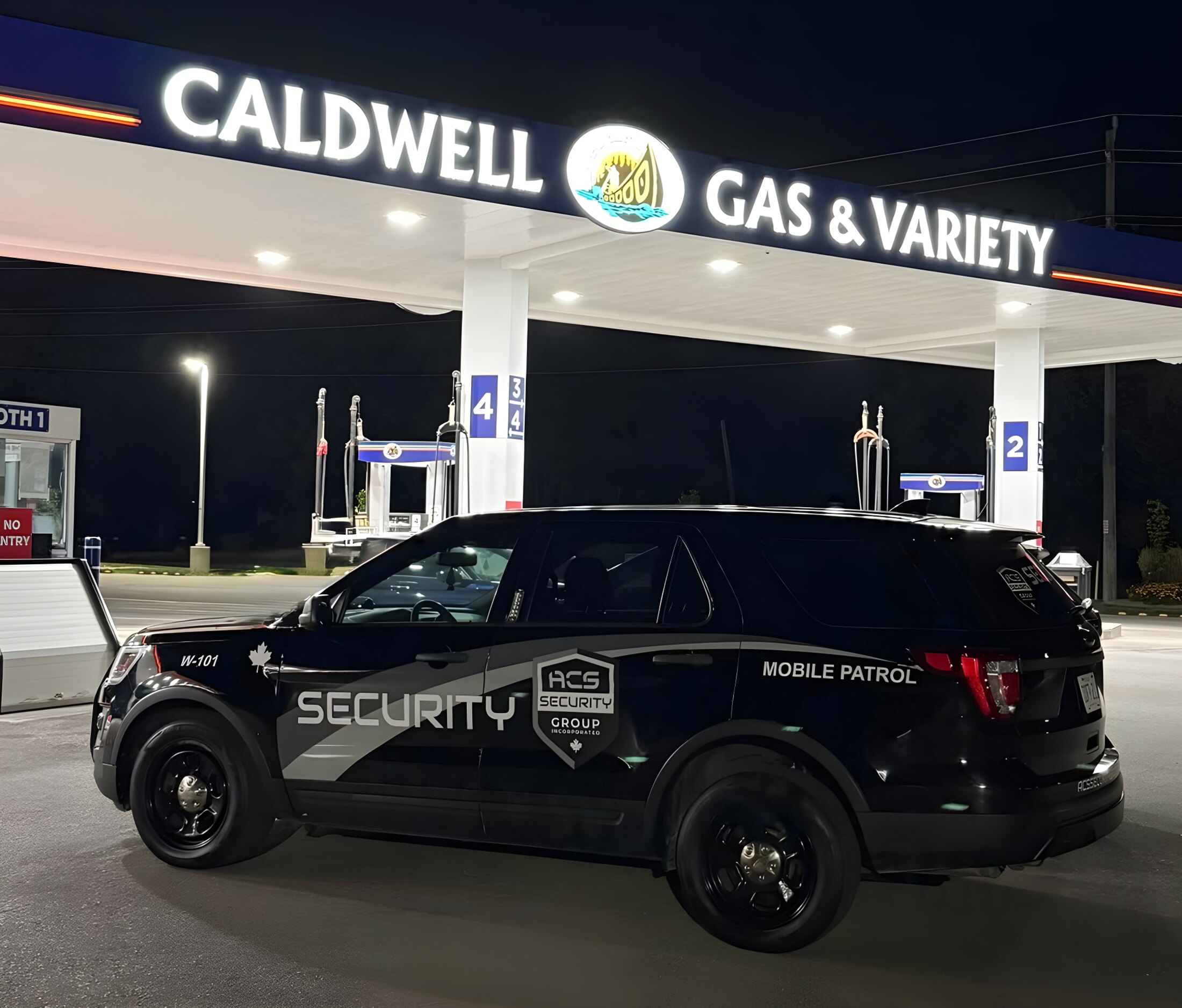 An ACS black Ford Explorer mobile patrol vehicle, unit W-101, parked at night under a lit gas-station canopy