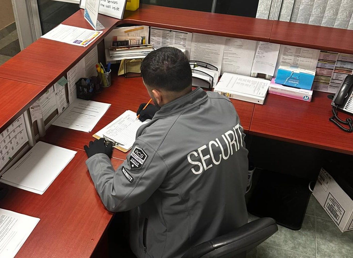 ACS security guard seated at a facility front desk completing a log report
