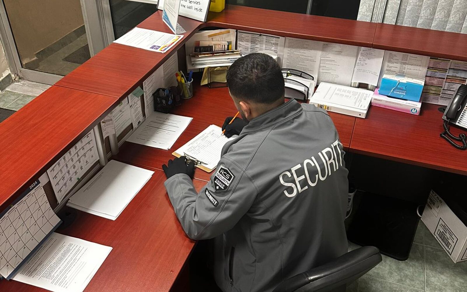 ACS security guard seated at a facility front desk completing a log report