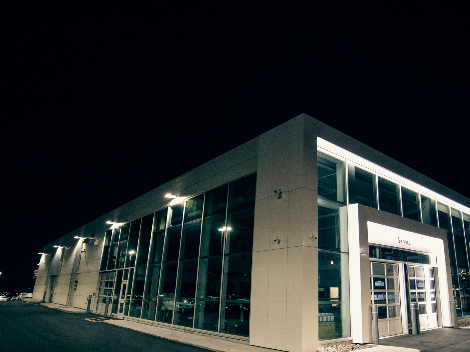 A glass-fronted dealership showroom lit from inside at night, with empty asphalt in front of it