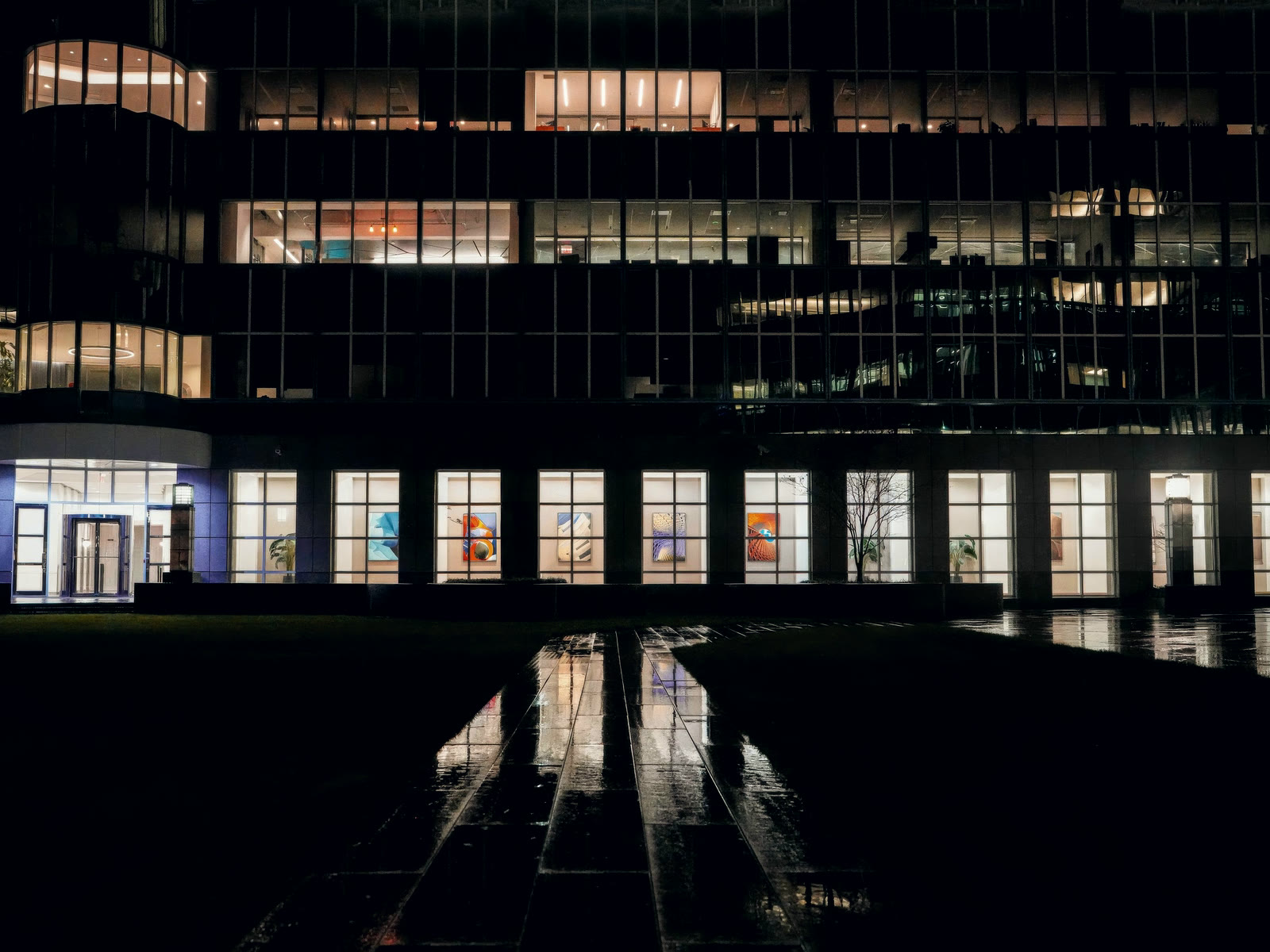 A two-storey commercial building at night, lit windows above a wet, empty forecourt