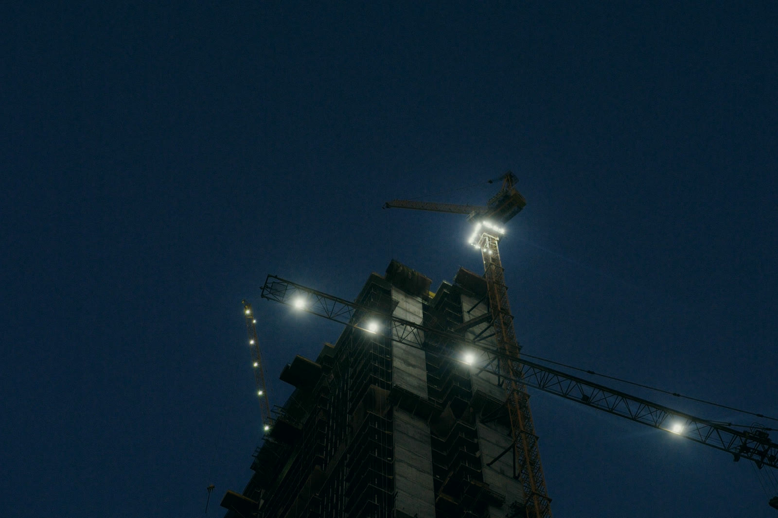 A building under construction at night, the tower crane lit above it