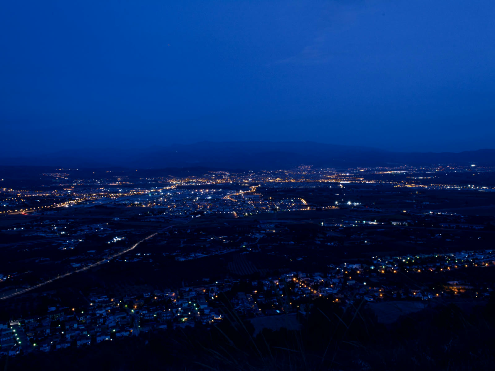 A lit district seen from the air at blue hour, buildings and roads running to the horizon