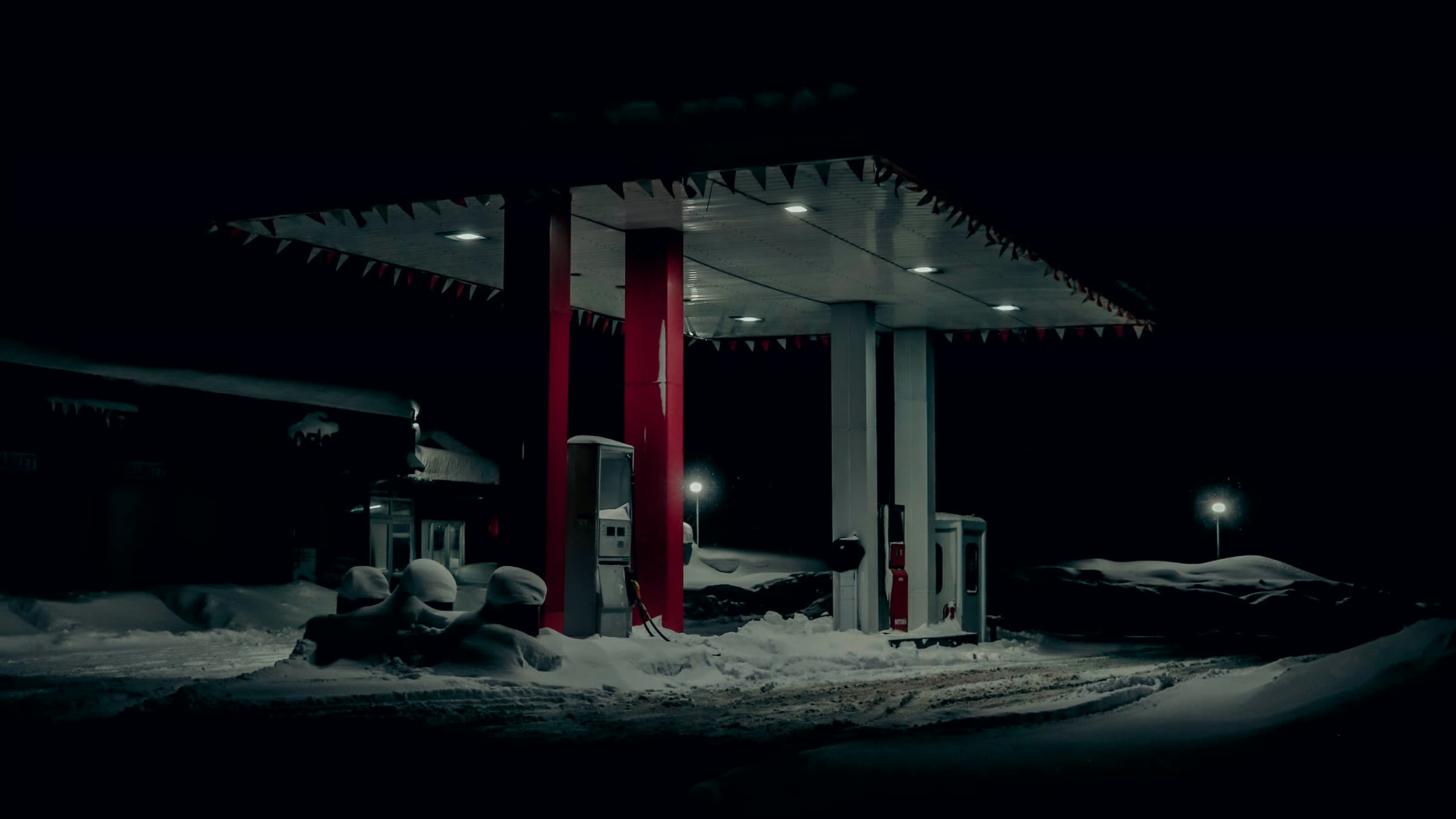 A fuel forecourt under a lit canopy at night, snow on the ground and nobody on it
