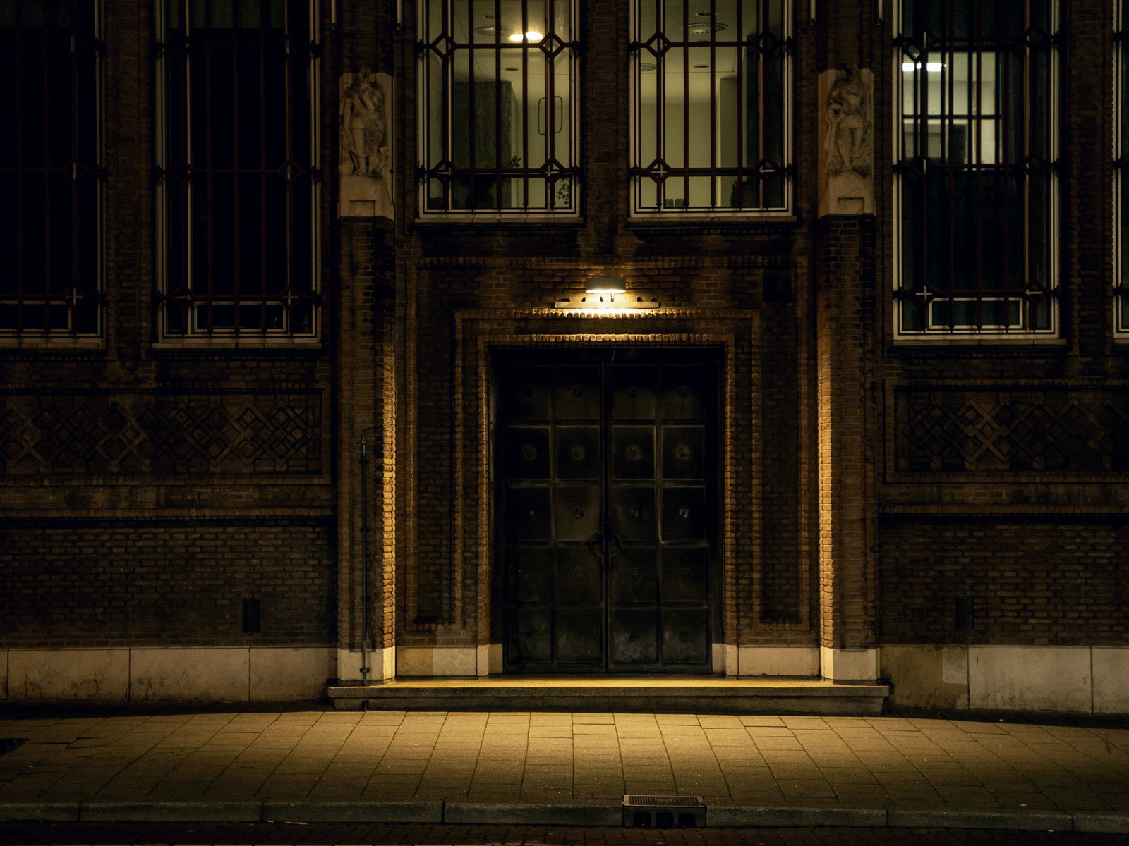 The lit doorway of a civic building at night, the pavement in front of it empty