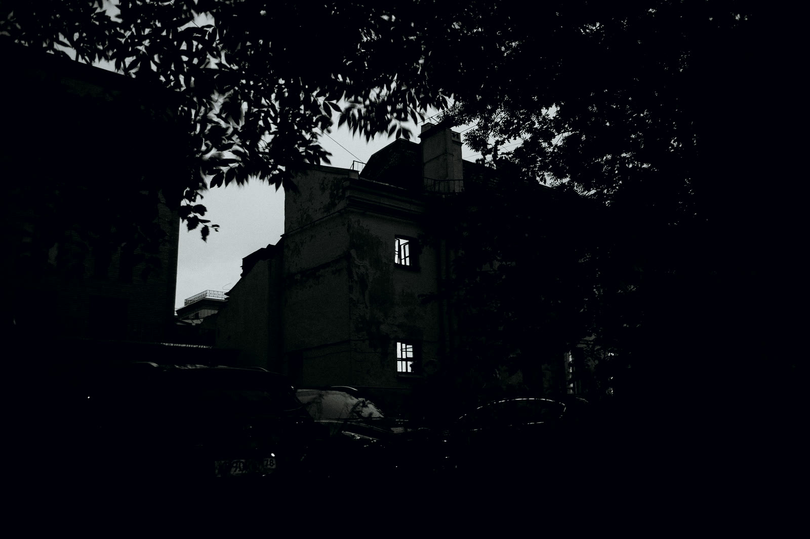 A dark empty house among trees with one window lit