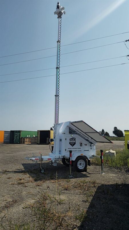 ACS mobile defense tower with its mast raised on a gravel yard beside shipping containers